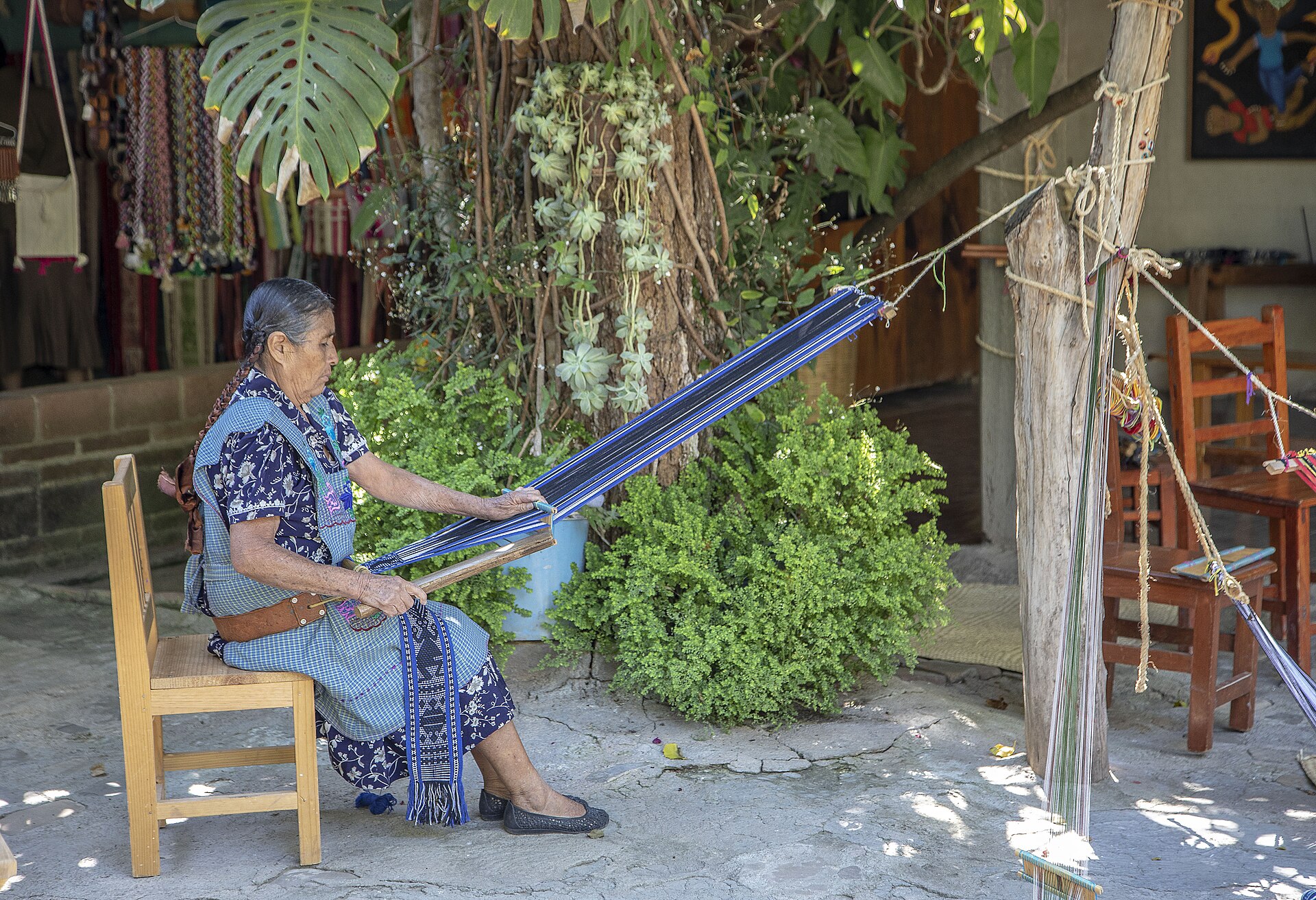 Mujer tejiendo en telar de cintura sentada en una silla al aire libre